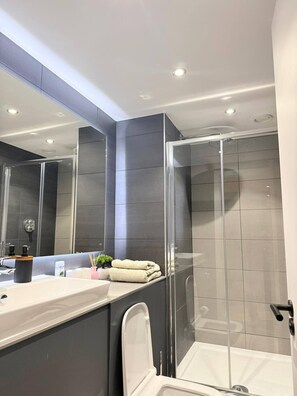 Ein modernes Badezimmer mit einer Duschkabine aus Glas, einem großen Spiegel und einem Waschtisch mit Spüle und Handtuchhalter.