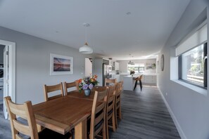 Une cuisine moderne avec des meubles blancs, un coin repas doté d’une table et de chaises en bois, et une vue sur le salon.