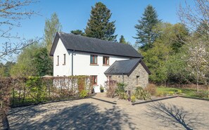 Une maison à deux étages avec une extension en pierre, entourée d’arbres et d’un jardin.