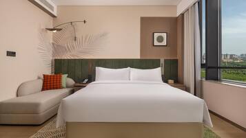 Quarto de hotel moderno com uma cama grande, área de estar, telefone fixado na parede e janela com vista para a cidade.
