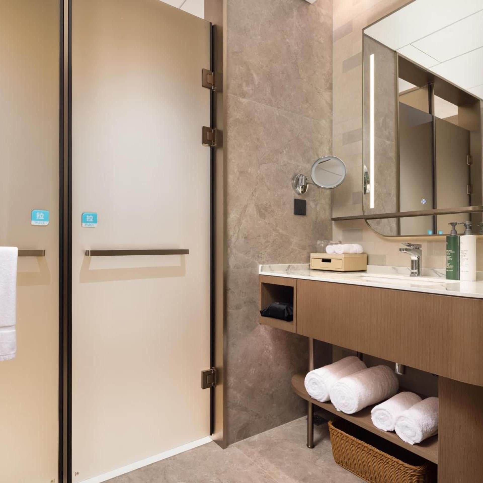 Un baño moderno con mampara de vidrio, tocador de madera, espejo y toallero.