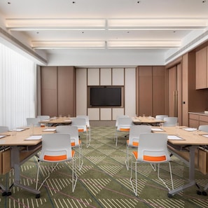 A conference room with a large flat-screen TV, white chairs with orange accents, and a patterned carpet.