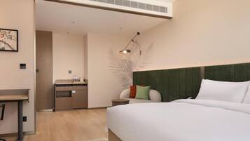 Habitación de hotel moderna con una cama grande, un escritorio, una silla, una mesita, una mesita de noche y una lámpara de pared.