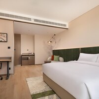 Habitación de hotel moderna con una cama grande, un escritorio, una silla, una mesita, una mesita de noche y una lámpara de pared.