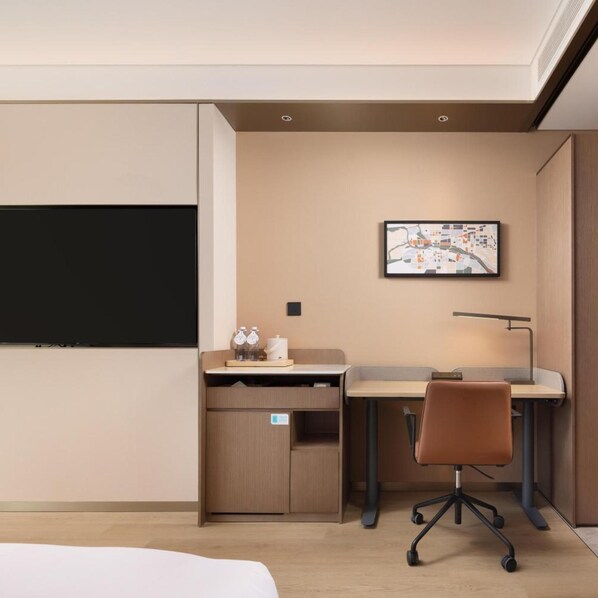 A hotel room with a bed, a desk, a chair, a television, and a wall-mounted artwork.