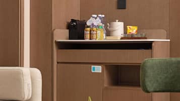 Une petite cuisine équipée comprenant une machine à café, des bouteilles et une bouilloire posées sur le plan de travail.