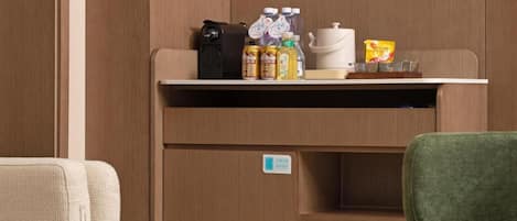 A compact kitchenette with a coffee machine, bottles, and a kettle on the countertop.