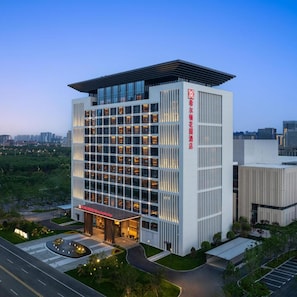 A modern hotel building with a prominent entrance, multiple floors, and a parking area.