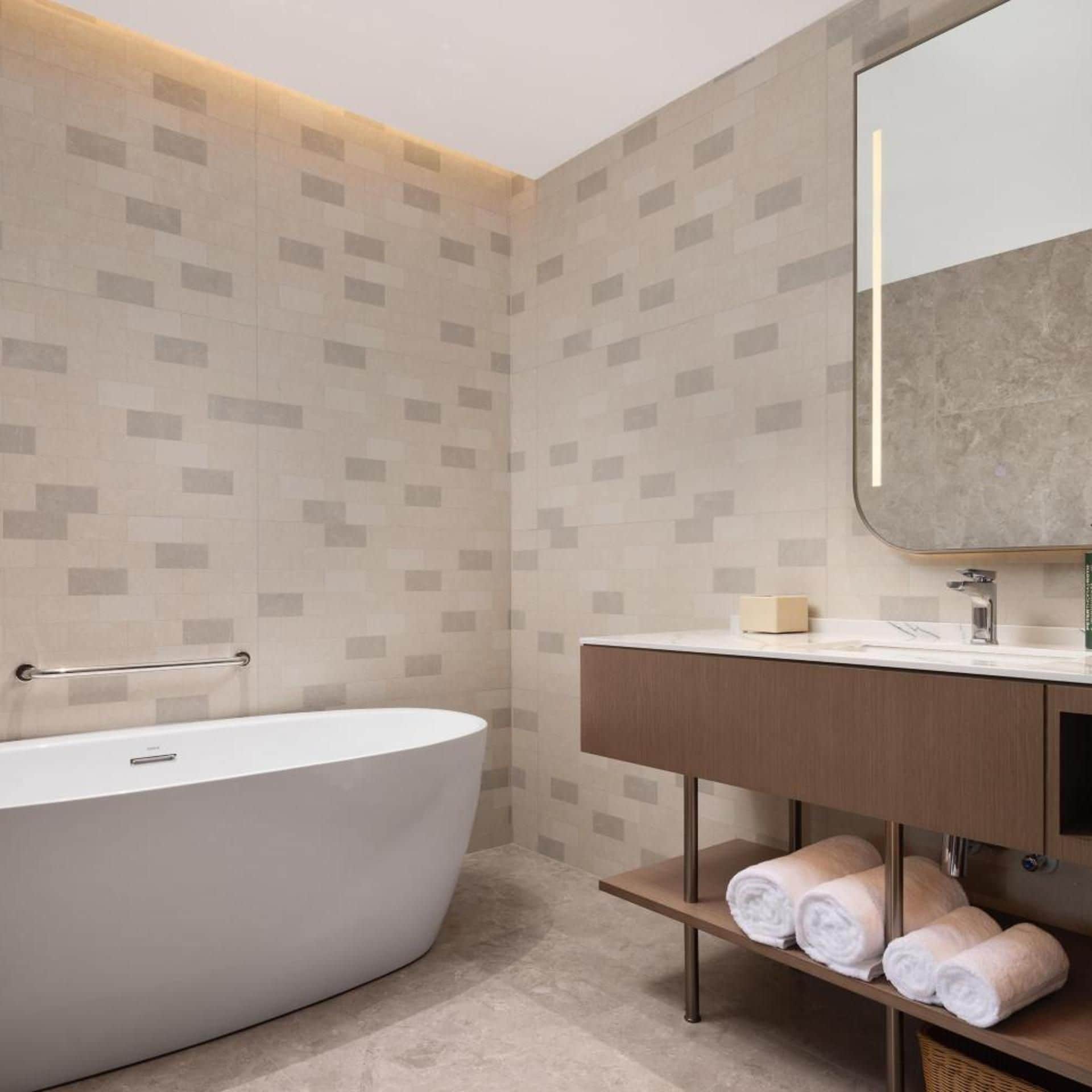 A modern bathroom with a freestanding bathtub, a vanity with a mirror, and a shelf with towels.