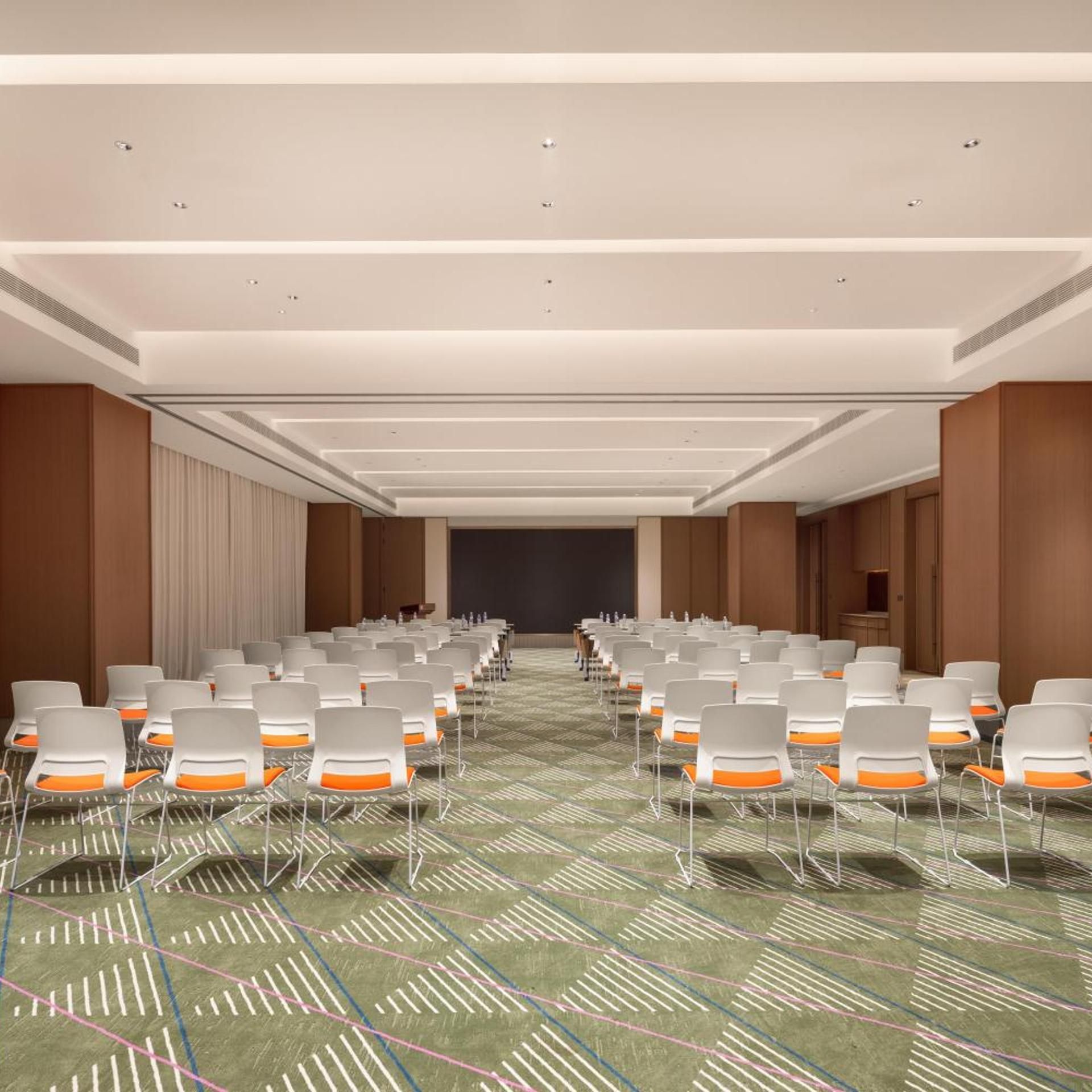 A conference room with rows of chairs, a projector screen, and a carpeted floor.