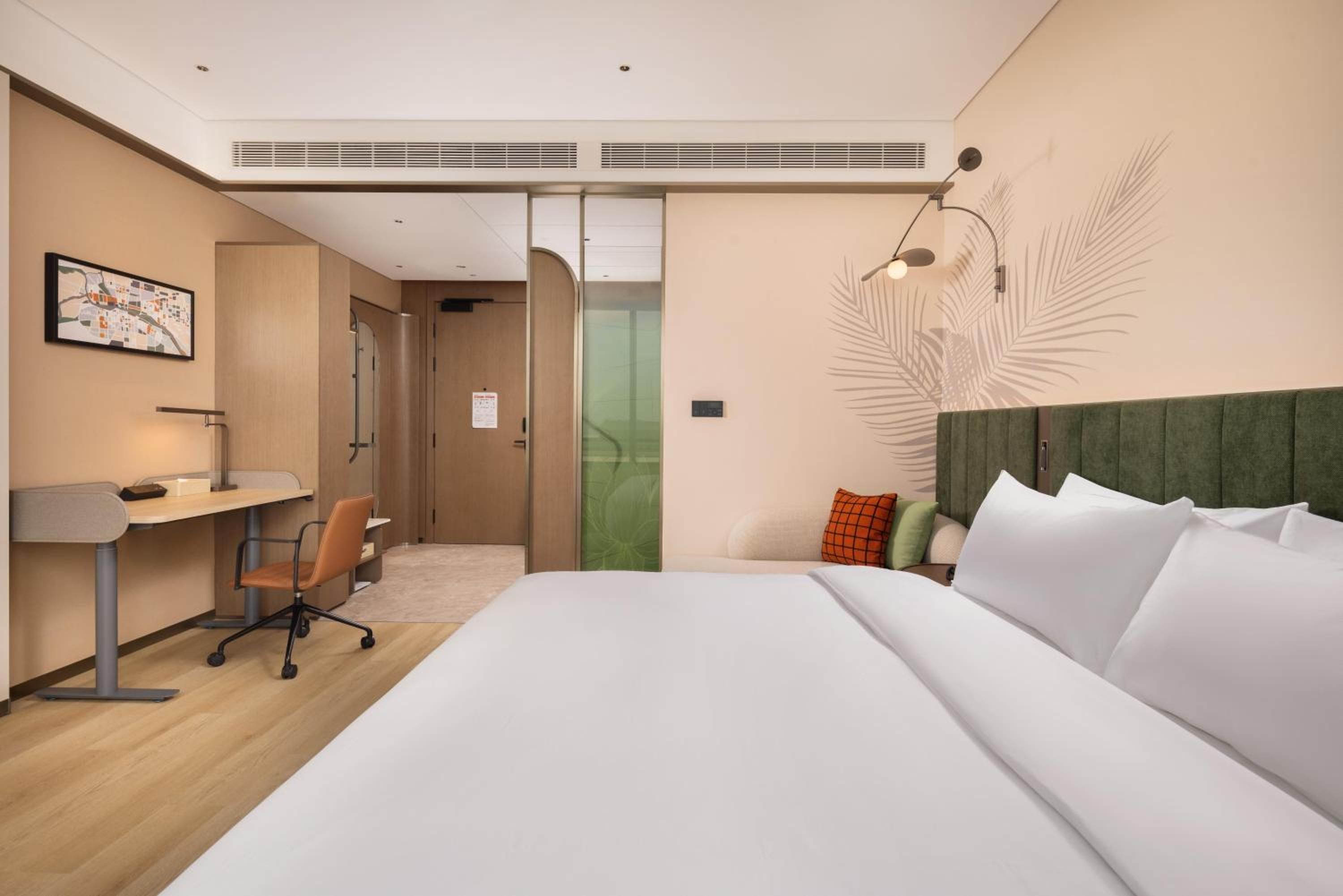 A hotel room with a bed, desk, chair, and a wall-mounted light fixture.