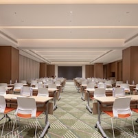 Sala de conferência com mesas e cadeiras dispostas em fileiras, equipada com garrafas de água e placas de identificação.