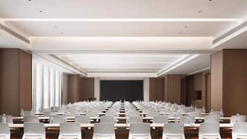 A conference room with rows of tables and chairs, a projector screen, and a carpeted floor.