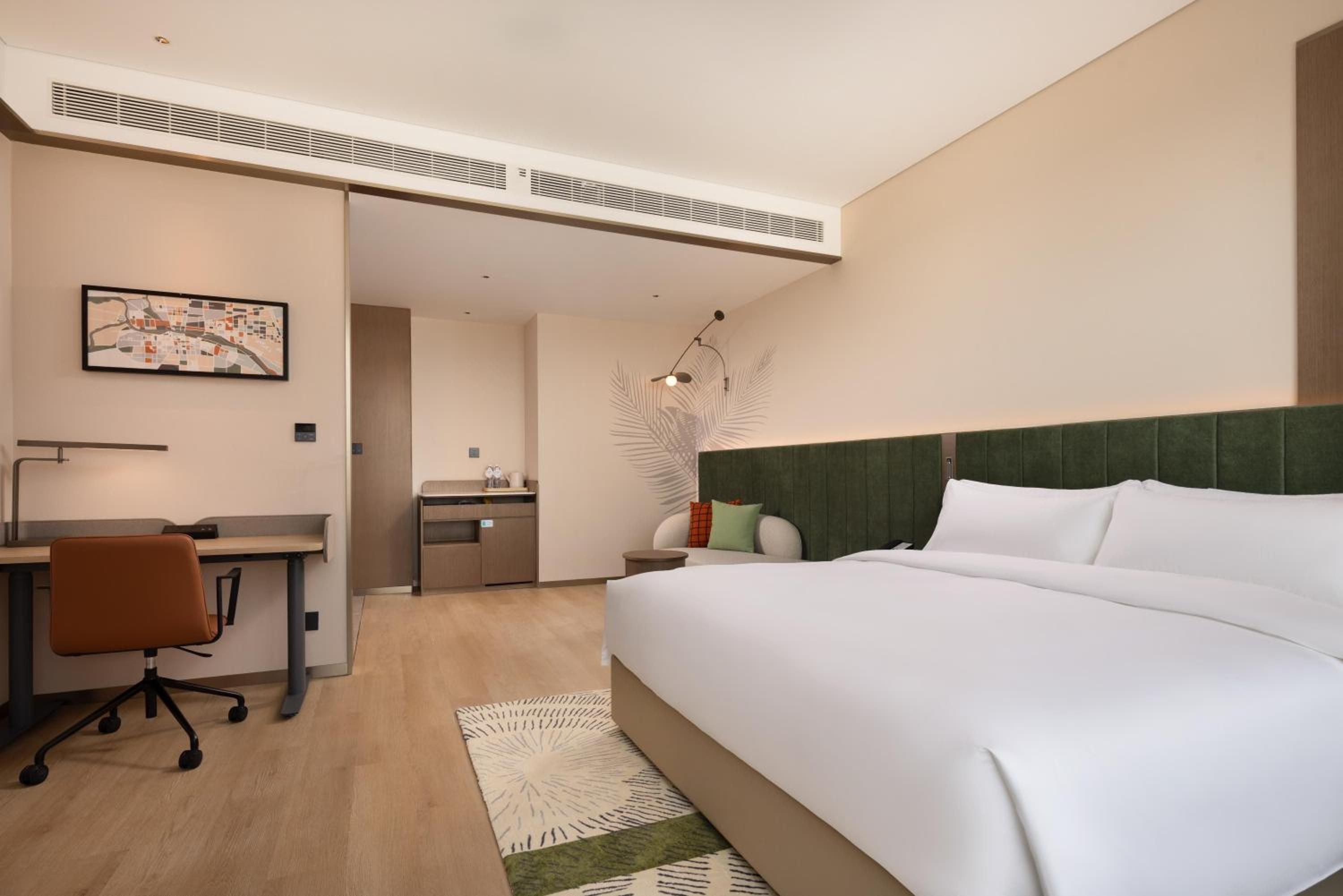 A hotel room with a bed, desk, chair, and a map on the wall.