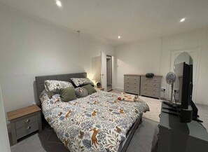 Ein Schlafzimmer mit einem großen Bett, einem Schminktisch, einem Spiegel und einem Fernseher.