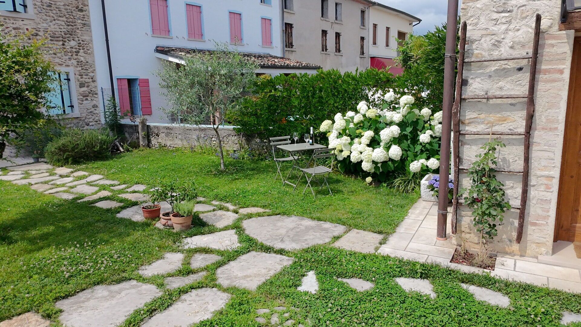 Une cour avec des allées pavées, des plantes en pot et une table entourée de chaises.