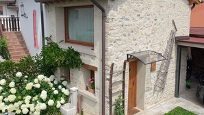 Ein Steinhaus mit Ziegeldach, einer Holztreppe und einem kleinen Garten mit weißen Blüten.