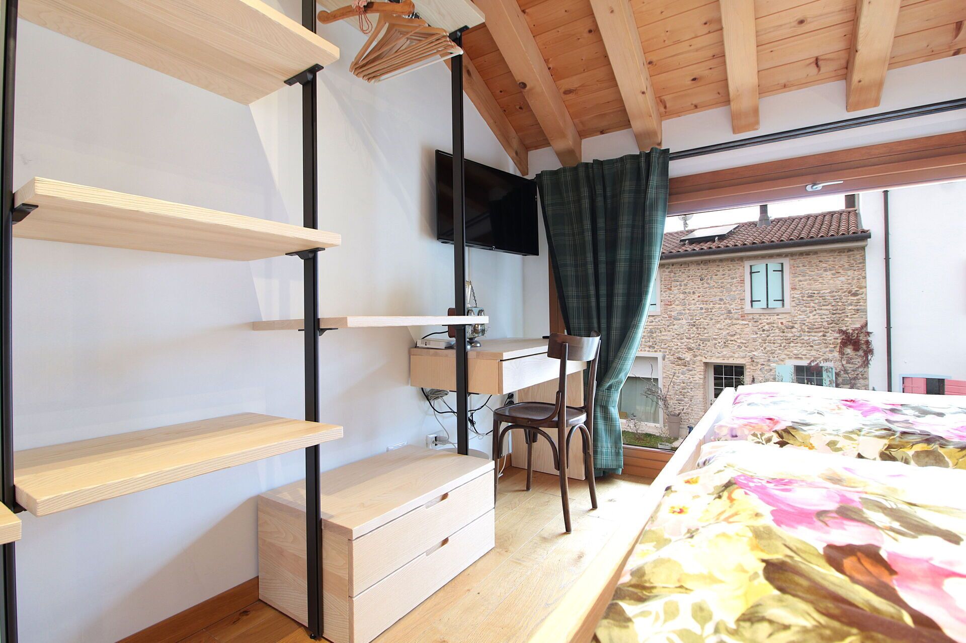 Ein Schlafzimmer mit Hochbett, Schreibtisch mit Stuhl, Fernseher und Blick auf ein Steinhaus.