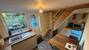 Een compacte keuken met een visgraatvloer, een houten aanrechtblad en uitzicht op de tuin door een raam.