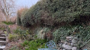 Een tuin met een stenen muur, een metalen tafel en stoelen, en een grindpad.