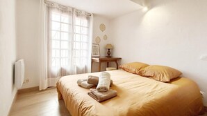 Un dormitori amb llit, una tauleta de nit, una làmpada i una finestra amb cortines.