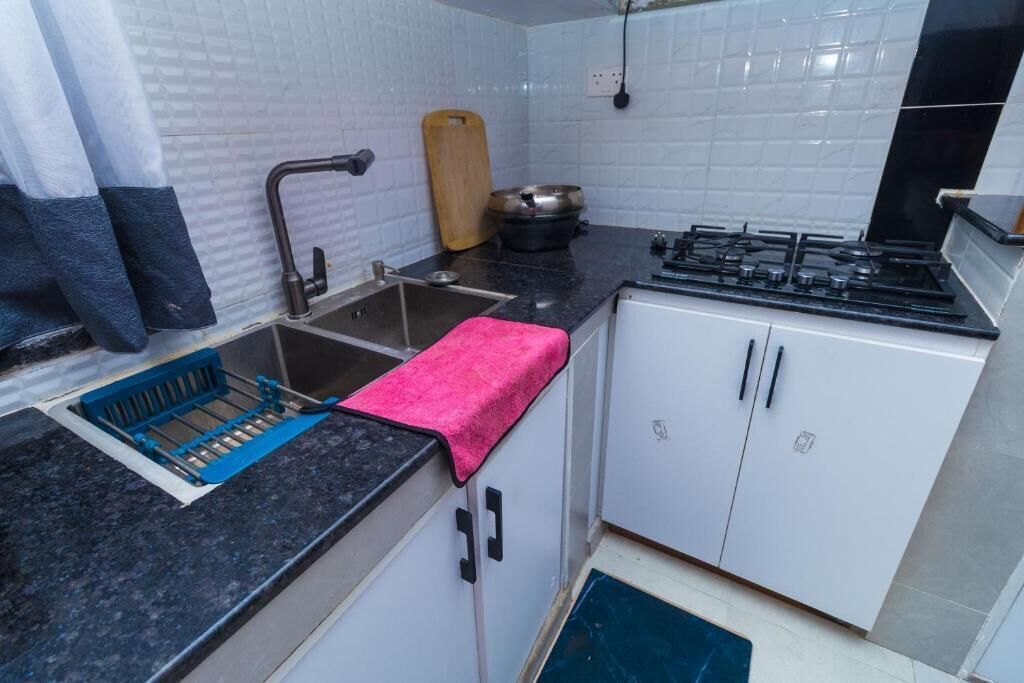 A compact kitchen with a gas stove, a sink with a blue drying rack, and white cabinets.
