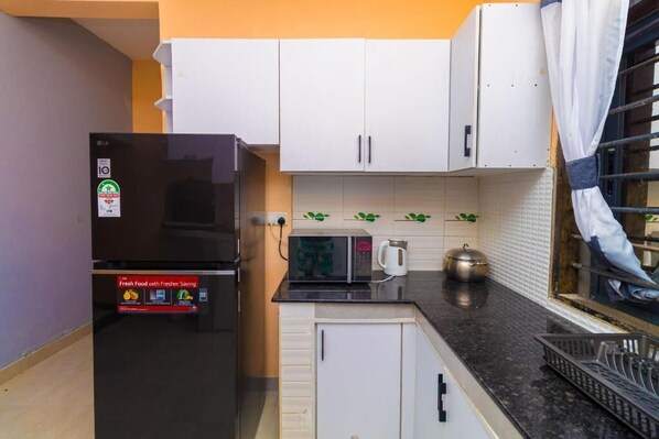 A compact kitchen with white cabinets, a black refrigerator, a microwave, and a kettle on the countertop.