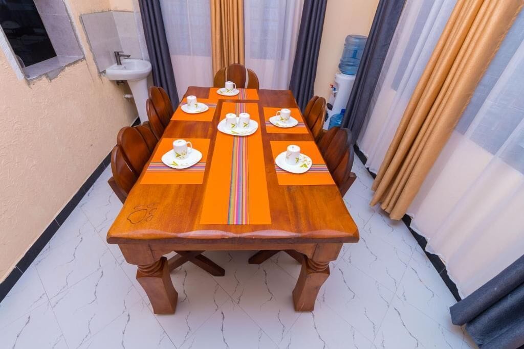 A dining table with six chairs, a sink, and curtains in a room with tiled flooring.