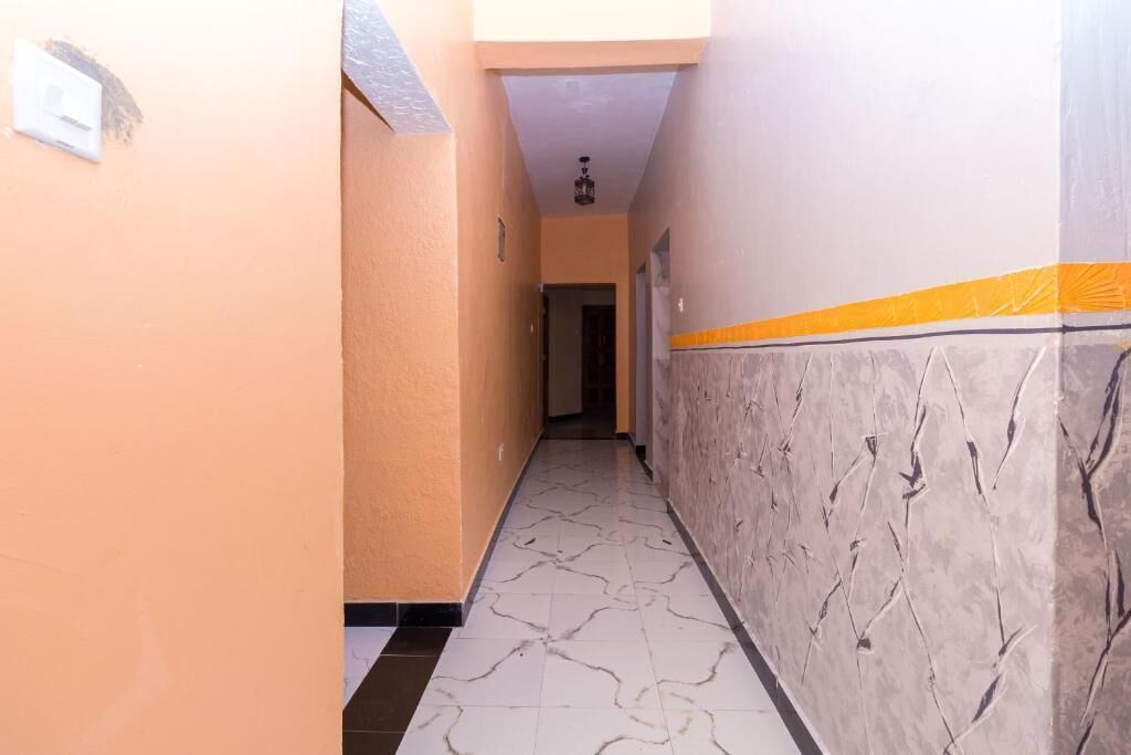 Un pasillo con piso de mármol, pared de color claro con textura y una franja amarilla cerca del techo.