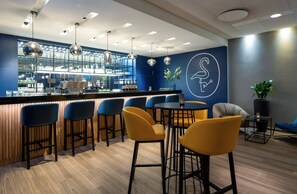 A bar area with stools, a counter, and a wall with a logo. - Voco Dusseldorf Seestern An Ihg Hotel (Düsseldorf)