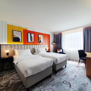 A hotel room with two beds, a desk, and a chair. There are two bedside tables with lamps. The room has a large window with curtains. - Voco Dusseldorf Seestern An Ihg Hotel (Düsseldorf)