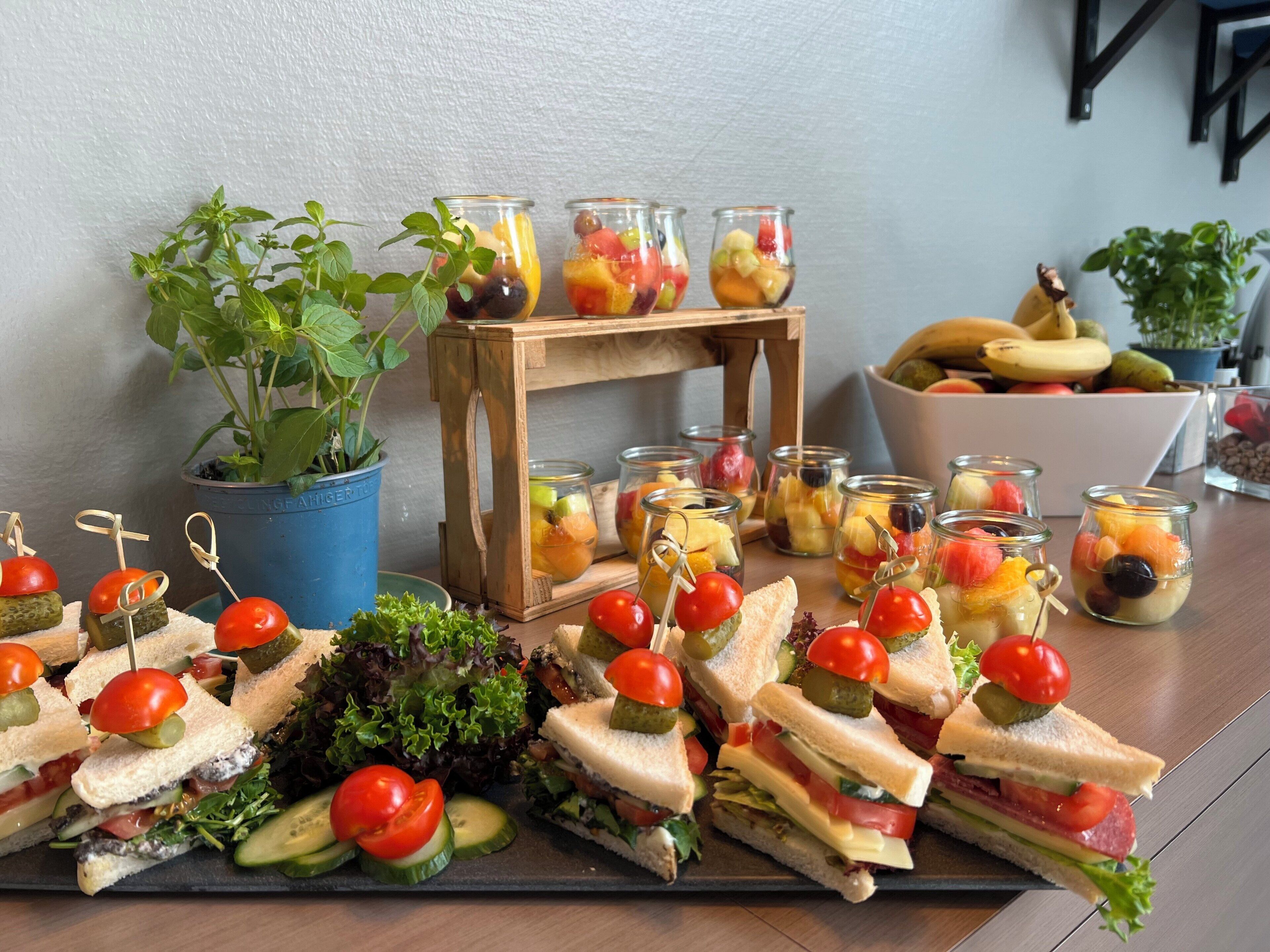 A table with sandwiches, fruit skewers, and a small plant.