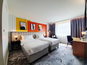 A hotel room with two beds, a desk, and a chair. There are wall-mounted lamps and a large window with curtains. - Voco Dusseldorf Seestern An Ihg Hotel (Düsseldorf)