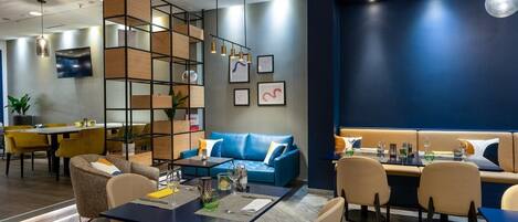Ein moderner Lounge-Bereich mit einem blauen Sofa, einem Esstisch mit Stühlen und einem Holzregal.