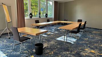 Ein Konferenzraum mit einem großen Tisch, Stühlen, einem Projektorständer und Blick auf Bäume durch die Fenster.