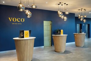 A reception area with a blue wall, wooden reception desks, and hanging spherical light fixtures. - Voco Dusseldorf Seestern An Ihg Hotel (Düsseldorf)