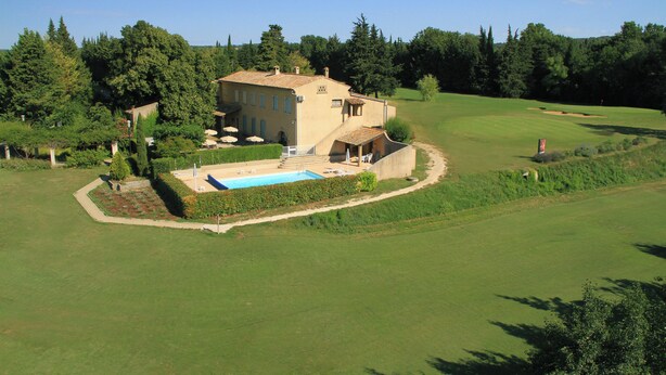 A large house with a swimming pool, surrounded by a golf course and lush greenery.