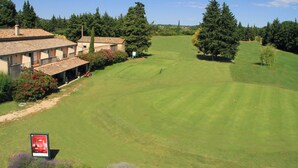A golf course with a clubhouse, surrounded by trees and a clear sky.