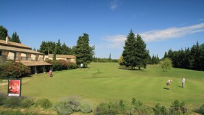 A golf course with a clubhouse, trees, and a clear sky.
