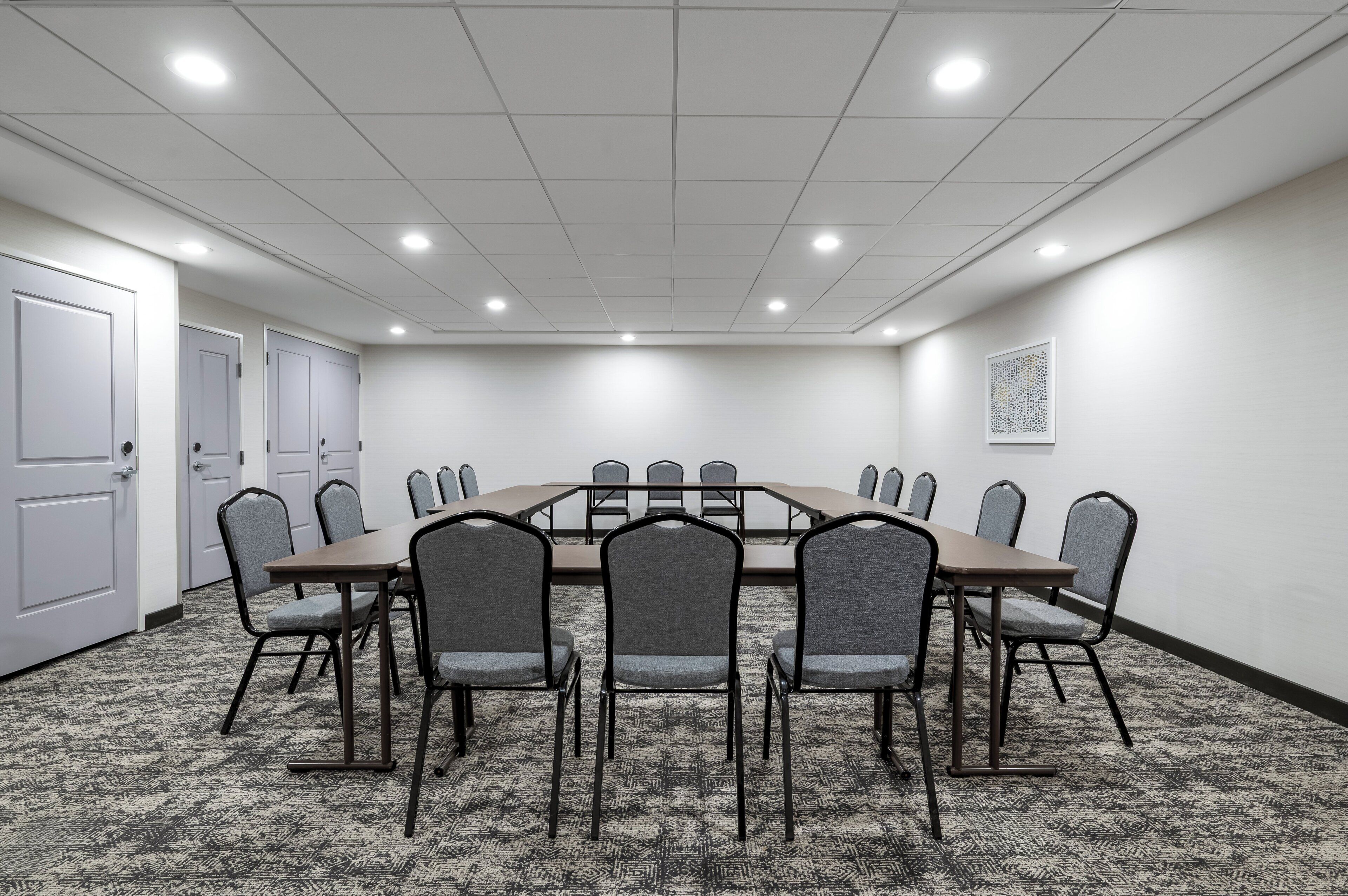 A conference room with a rectangular table, eight chairs, a carpeted floor, and a ceiling with recessed lighting.