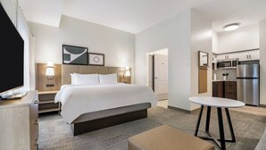 Een hotelkamer met een bed, nachtkastje, lamp en uitzicht op de keuken.