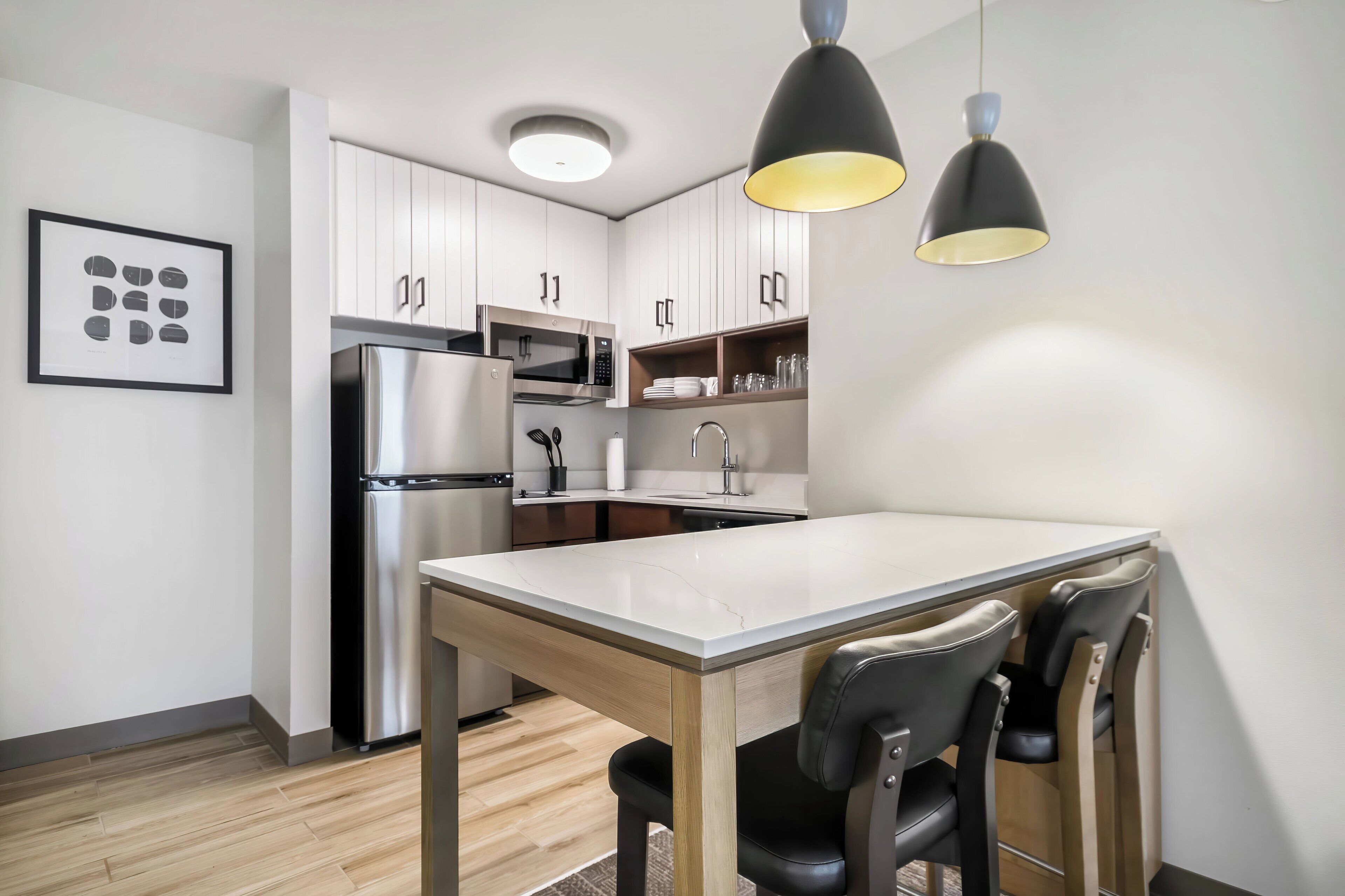 Una cocina moderna con armarios blancos, electrodomésticos de acero inoxidable, una mesa de comedor con sillas e iluminación colgante.