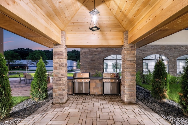 Eine Terrasse im Freien mit Kamin aus Stein, Grill und überdachter Sitzgruppe.