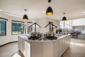 Uma cozinha moderna com uma ilha central, iluminação pendente e vista para o exterior através de grandes janelas.