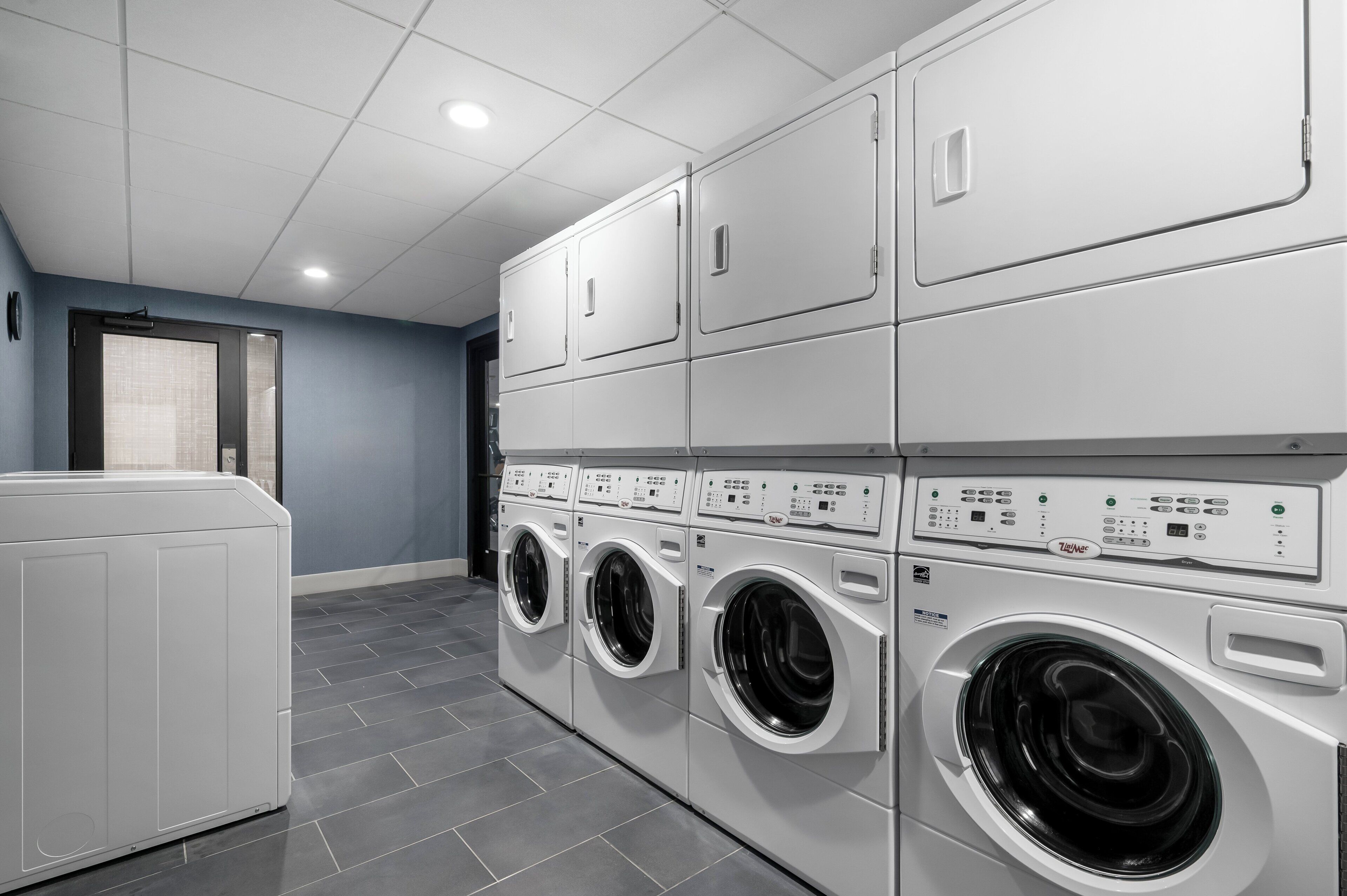 A laundry room with a front-loading washer and dryer, a tiled floor, and a blue accent wall.
