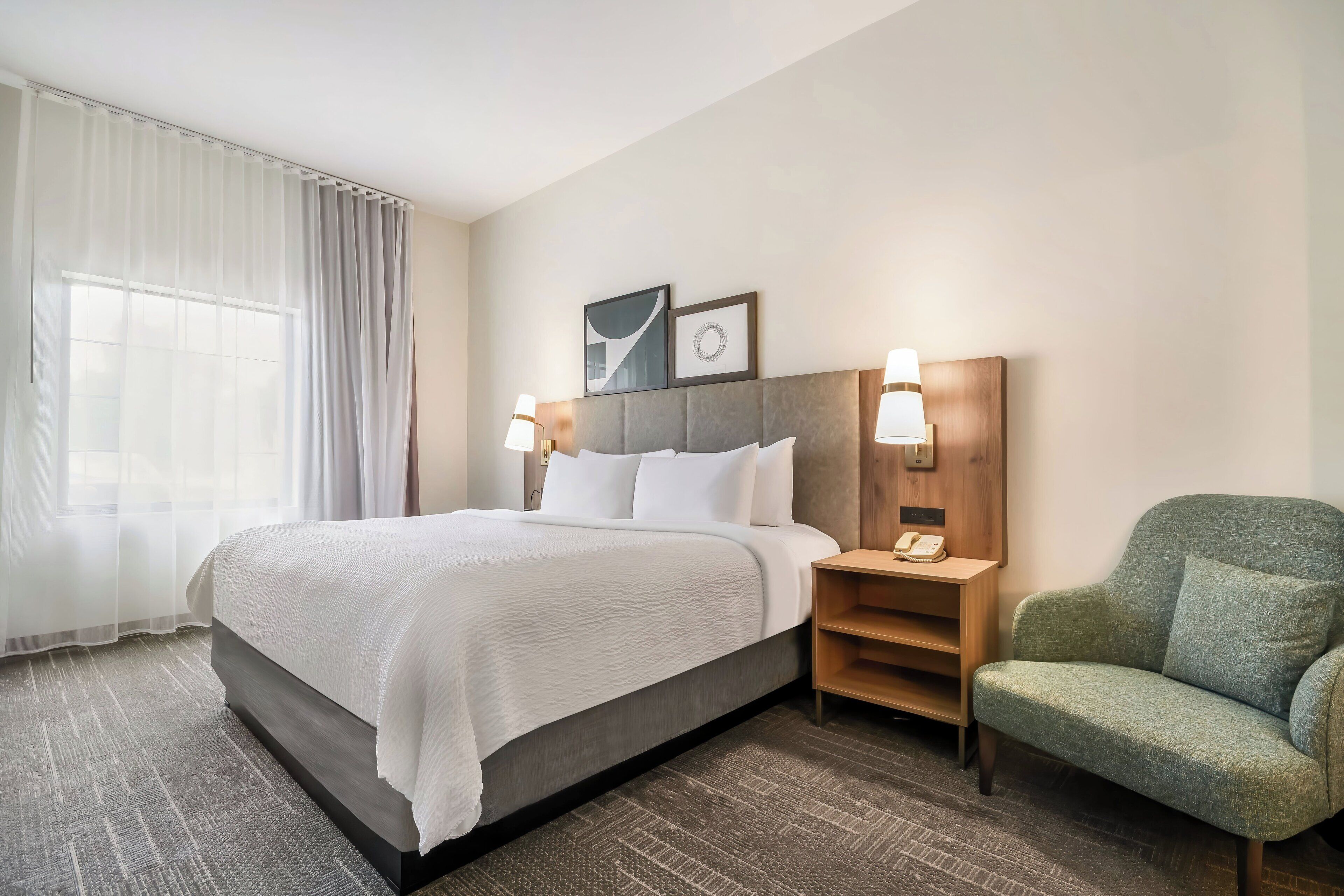 Een hotelkamer met een bed, een stoel, een nachtkastje en een raam met gordijnen.