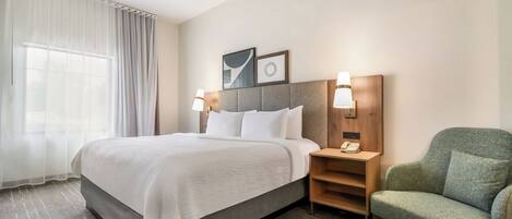 A hotel room with a bed, a chair, a nightstand, and a window with curtains.