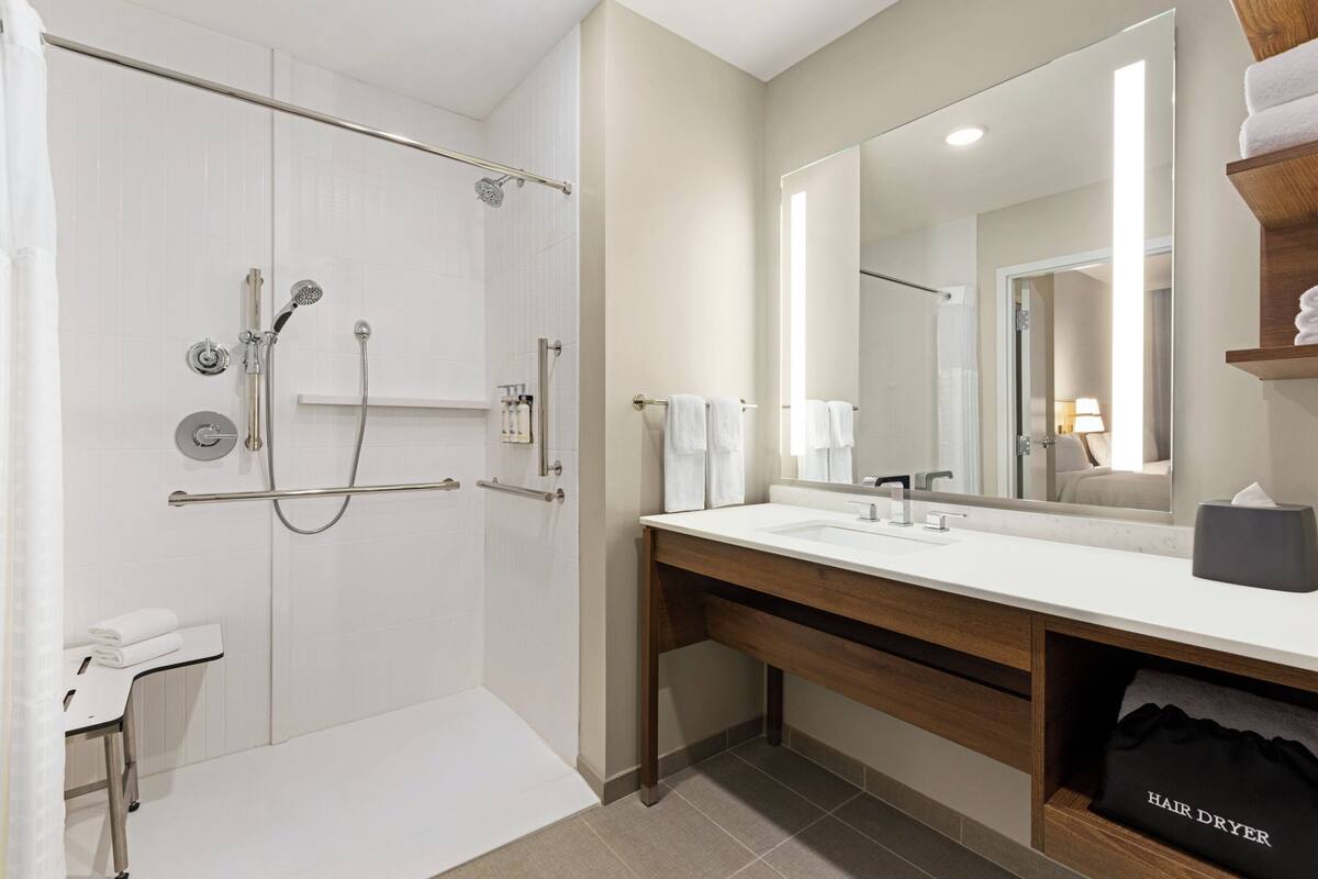 Ein modernes Badezimmer mit barrierefreier Dusche, einem Waschtisch mit Spiegel und einem Handtuchhalter.
