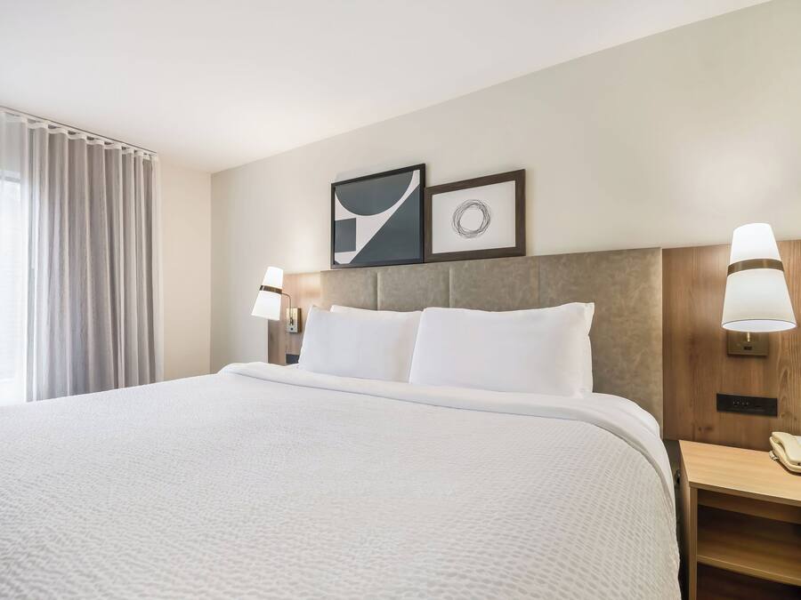 A hotel room with a large bed, two wall-mounted lamps, a bedside telephone, and two framed pictures on the wall.