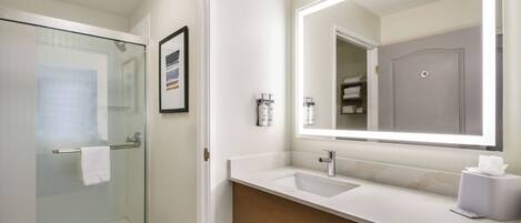 Une salle de bain moderne avec une douche à parois de verre, un lavabo blanc avec un miroir et un meuble-lavabo en bois.